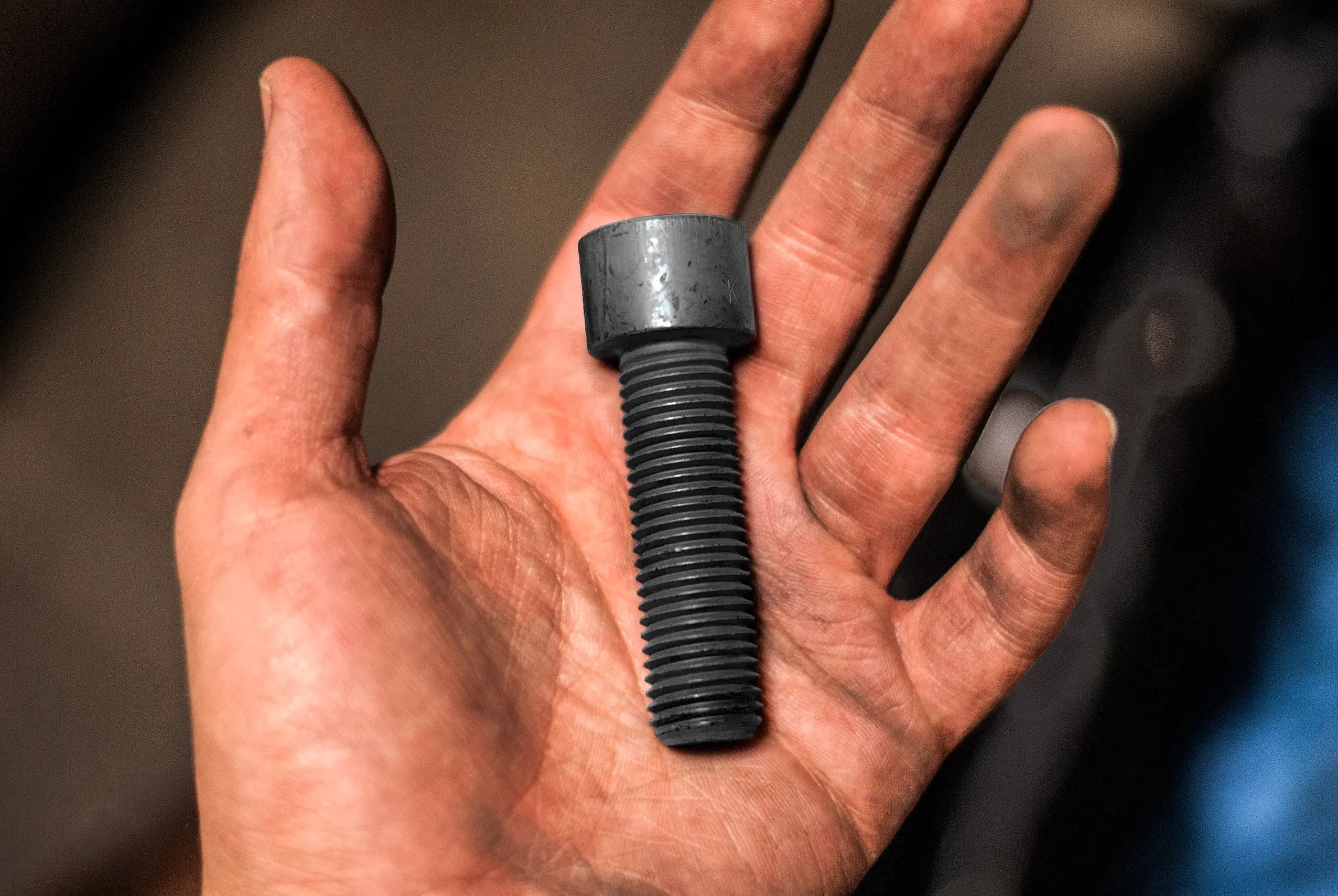 Black socket head cap screw resting in a worker's open hand
