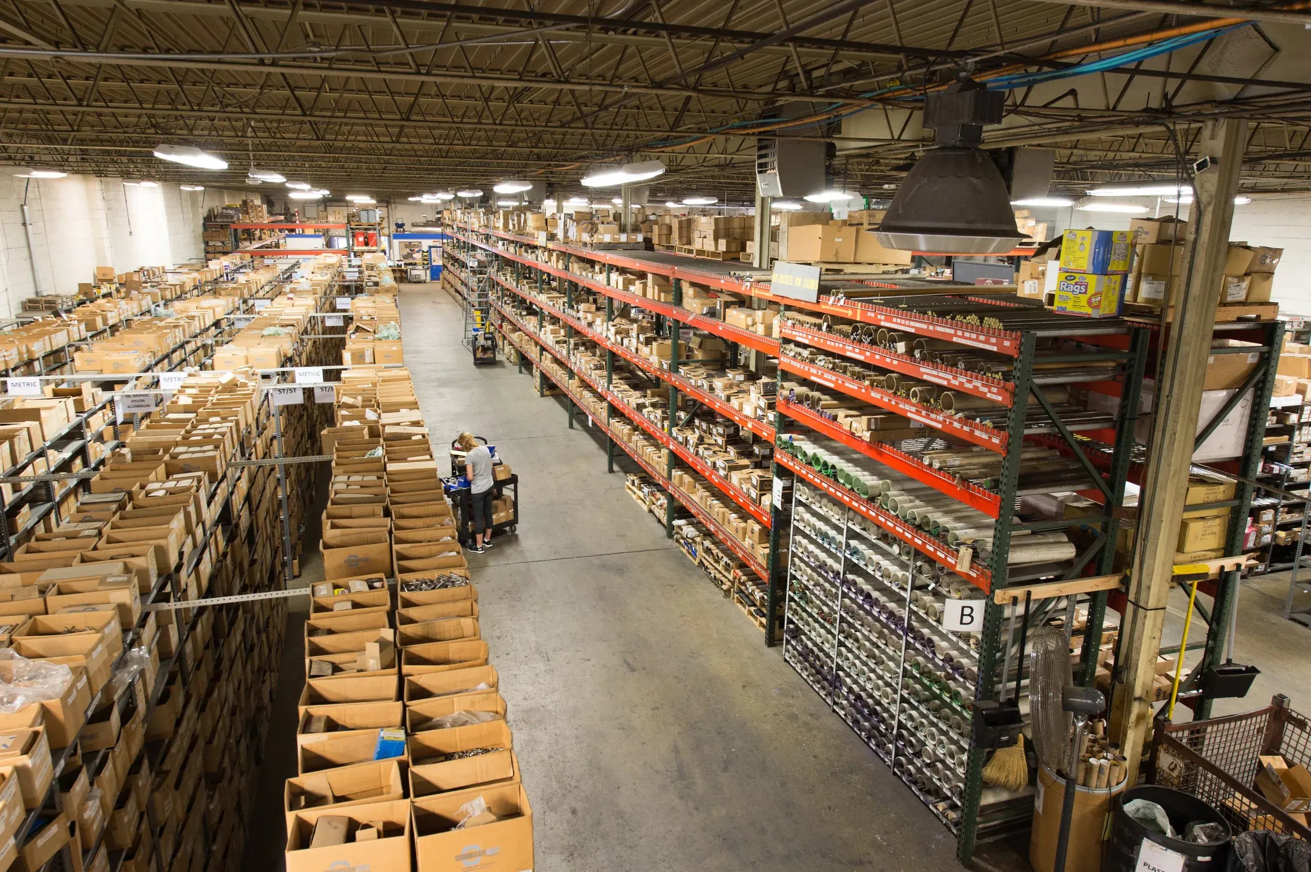 Employee pulling fasteners from boxed bin shelving in a warehouse aisle