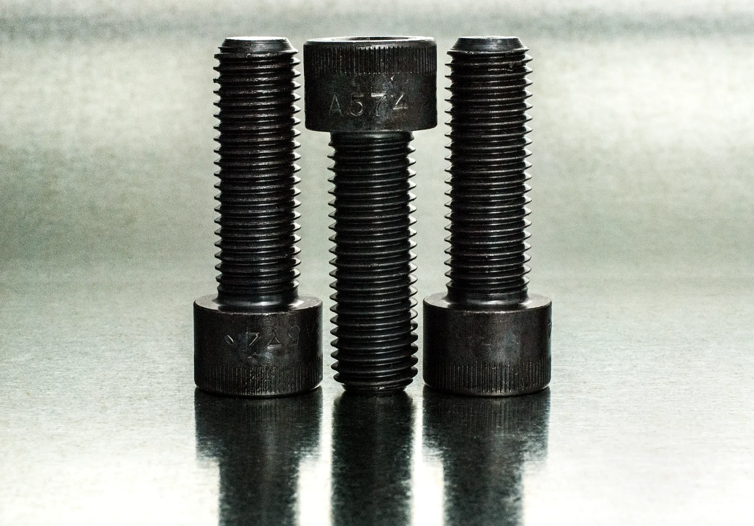 Three black A574 socket head cap screws on a reflective steel surface