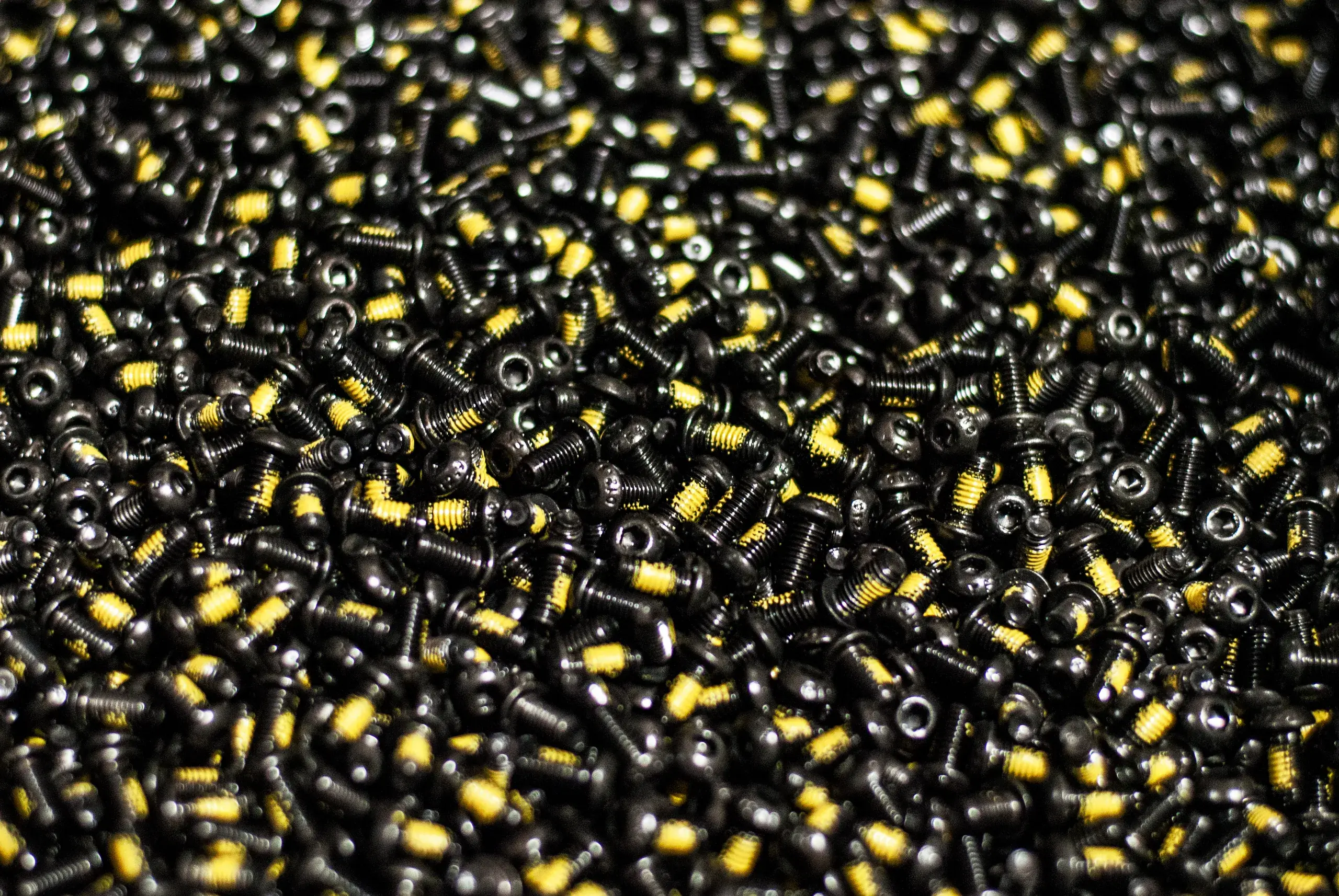 Pile of black button head socket screws with yellow thread-locking patches
